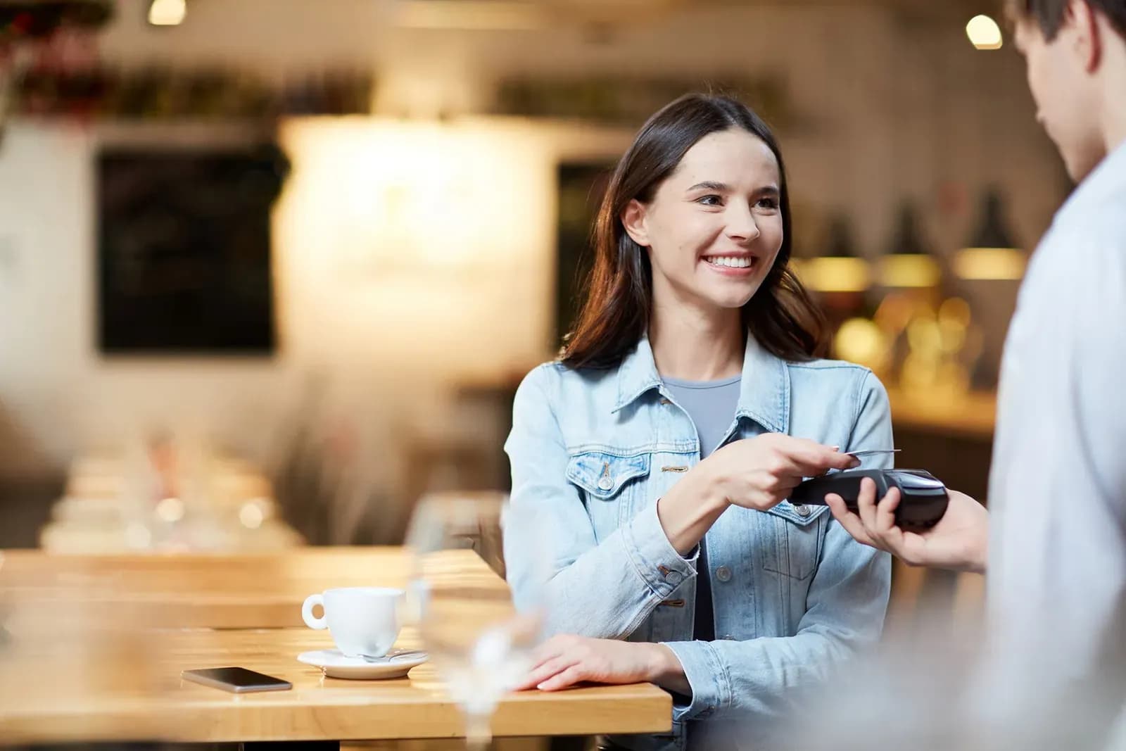 Customer in a café paying by card on a handheld terminal held by the waiter